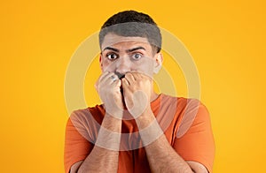 Scared frightened brazilian man biting his fists, holding hands next to mouth and looking at camera with wide open eyes