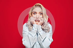 Scared girl biting fingernail,being terrible accident, isolated on red background. Frightened woman staring to you