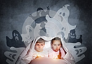 Scared girl and boy reading book in bed