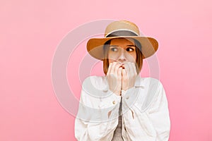 Scared girl in hat and shirt isolated on pink background, looks away with shocked face. Frightened lady lady, closeup portrait on