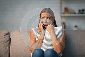 Scared Girl Holding Phone Embracing Pillow Sitting On Sofa Indoor