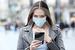 Scared girl with mask reading news on her phone on street