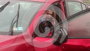 Scared girl talking on the phone after a car accident in the rain, car is broken