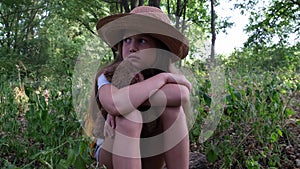 Scared girl with a teddy bear and yellow backpack sits alone in the thicket. Child tourist lost in the forest. Upset kid