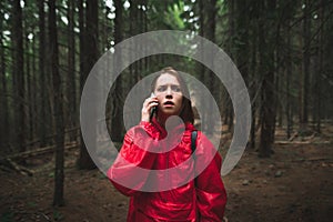 Scared hiker girl stands in dark forest on the trail and calls 911 on the phone. Shocked woman in red doodle stands in mountain