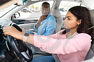Scared instructor looking at serious focused black lady driver