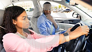Scared instructor looking at serious focused black lady driver