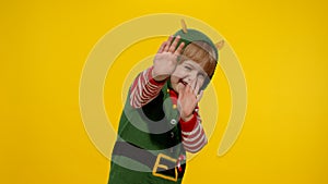 Scared kid girl in Christmas elf Santa helper costume looking aafraid, hiding face with hands