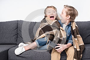 Scared kids in blanket sitting on sofa and looking at each other