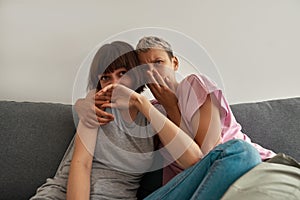 Scared lesbian girls watching TV on sofa at home