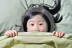 Scared little asian girl hiding behind blanket