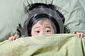 Scared little asian girl hiding behind blanket