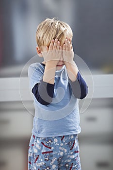 Scared little boy in casuals with hands over his eyes photo