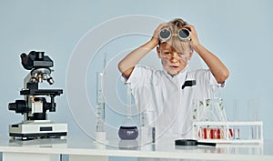 Scared little boy in coat playing a scientist in lab by using equipment