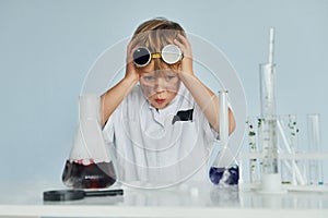 Scared little boy in coat playing a scientist in lab by using equipment