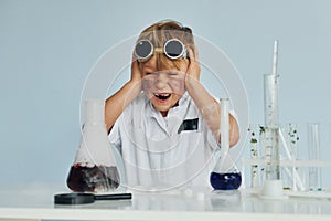 Scared little boy in coat playing a scientist in lab by using equipment