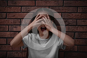 Scared little girl closing eyes with hands near brick wall. Child in danger