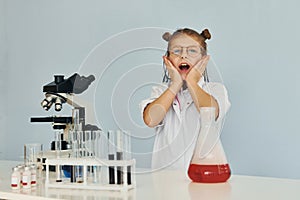 Scared little girl in coat playing a scientist in lab by using equipment