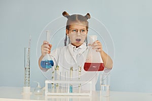 Scared little girl in coat playing a scientist in lab by using equipment