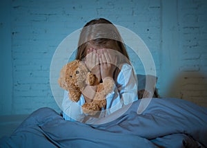 Scared little girl covering face with hands in fear in darkness at night