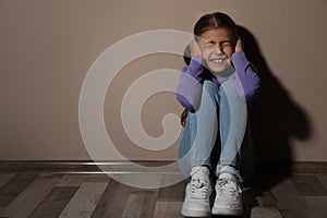 Scared little girl near beige wall. Domestic violence concept