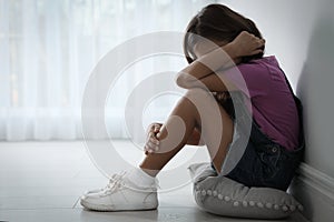 Scared little girl near white wall indoors. Domestic violence concept