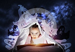 Scared little girl reading book in bed