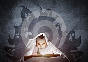 Scared little girl reading book in bed