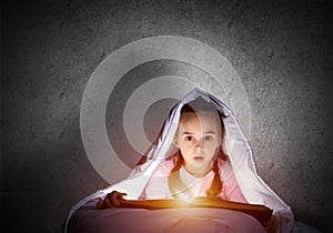 Scared little girl reading book in bed
