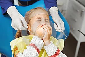 Scared little girl sits at dentist chair and covered her mouth from fear