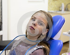 Scared little girl sitting in the dentist`s office. Portrait of a girl in a dental chair