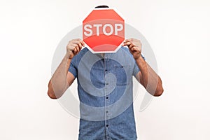 Scared man in blue shirt hiding face behind stop sign, victim of bullying, violence and discrimination