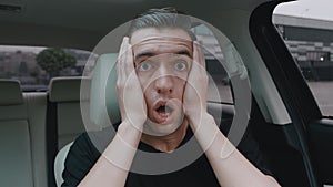Scared man driver looks into camera with startle at face clutches his head showing fear and surprise while sitting in a