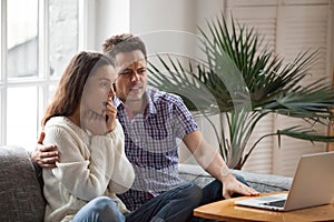 Scared man embracing shocked woman watching horror film on laptop