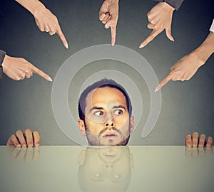 Scared man employee hiding under the table being accused by many people who point fingers at him photo