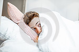 Scared man hiding under the bedsheets