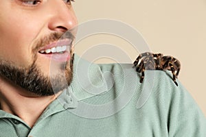 Scared man with tarantula on beige, closeup. Arachnophobia fear of spiders