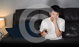 Scared man is watching horror movie TV on sofa at night