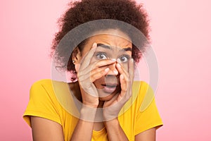 Scared millennial african american curly woman student in yellow t-shirt covering her face with hands and afraid