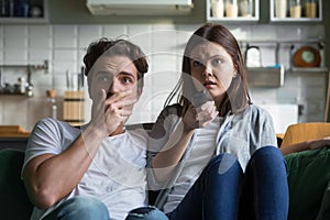 Scared millennial couple watching horror movie on tv at home