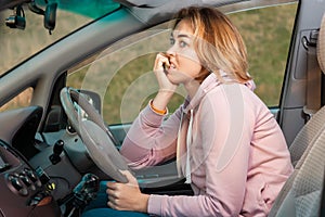 A scared nervous woman is sitting behind the wheel of a car and bites her nails. Side view. Fine for violation of