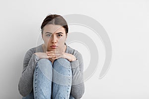 Scared sad worried millennial european woman sits on floor at home interior, on gray wall background