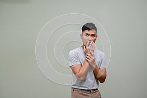 Scared and shocked millennial Asian man covering his mouth. isolated background