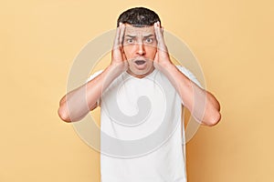 Scared shocked panicked man wearing white casual t-shirt standing isolated over beige background looking at camera with big full