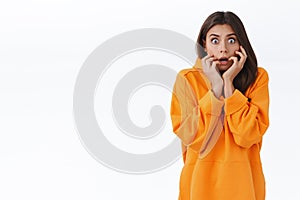 Scared and shocked speechless young woman in orange hoodie, gasping afraid staring camera, hear terrifying rumours