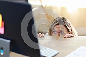 Scared and shocked woman in panic behind desk looking at computer screen.