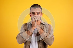 Scared shocked young caucasian man with beard in casual covers mouth with hands