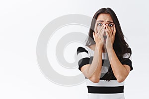 Scared and shocked young terrified asian brunette girl cover face with hands horrified, staring through fingers