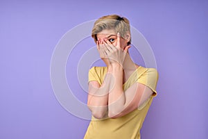 Scared short-haired female looking at camera through one eye, closing other eye
