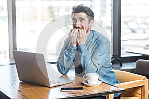 Scared! Side view portrait of emotional nervous young businessman in blue jeans shirt are sitting in cafe, working onlone and nail